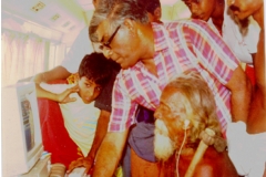 Prof. Samaranayajke, then Chairman, CINTEC demonstrating computer use to the Veddha Chief Tissahamy at Dambane, the Veddha village in 1990 using the equipment of the CINTEC mobile Computer Lab. Also in the picture are his sons Nayana and Samitha and Present Veddha Chief Vannialage Aththo. Son of Tissahamy.